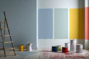 Interior room with paint samples tested on the wall, paint cans on the floor, and a ladder beside the workspace.