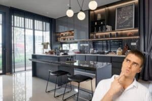 Modern luxury kitchen with dark cabinetry and marble countertops, featuring a person thoughtfully evaluating design choices.
